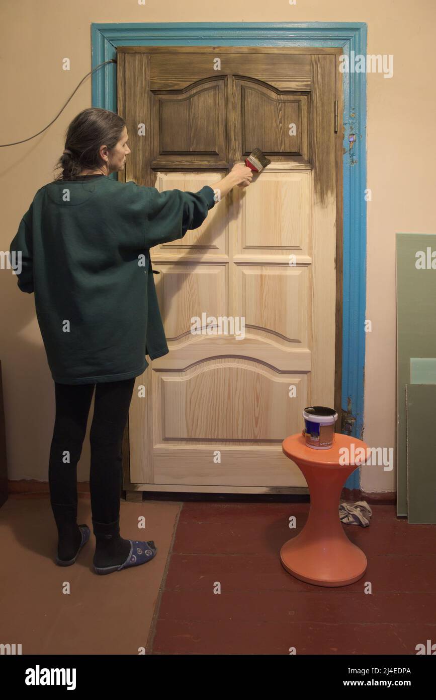 Riparazione nella vecchia casa. Donna dipinge la porta. Le nuove porte in legno sono installate al posto di quelle vecchie. Foto Stock