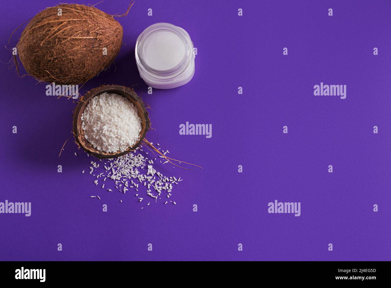 Cocco, fiocchi e olio di cocco in vaso su sfondo viola Foto Stock