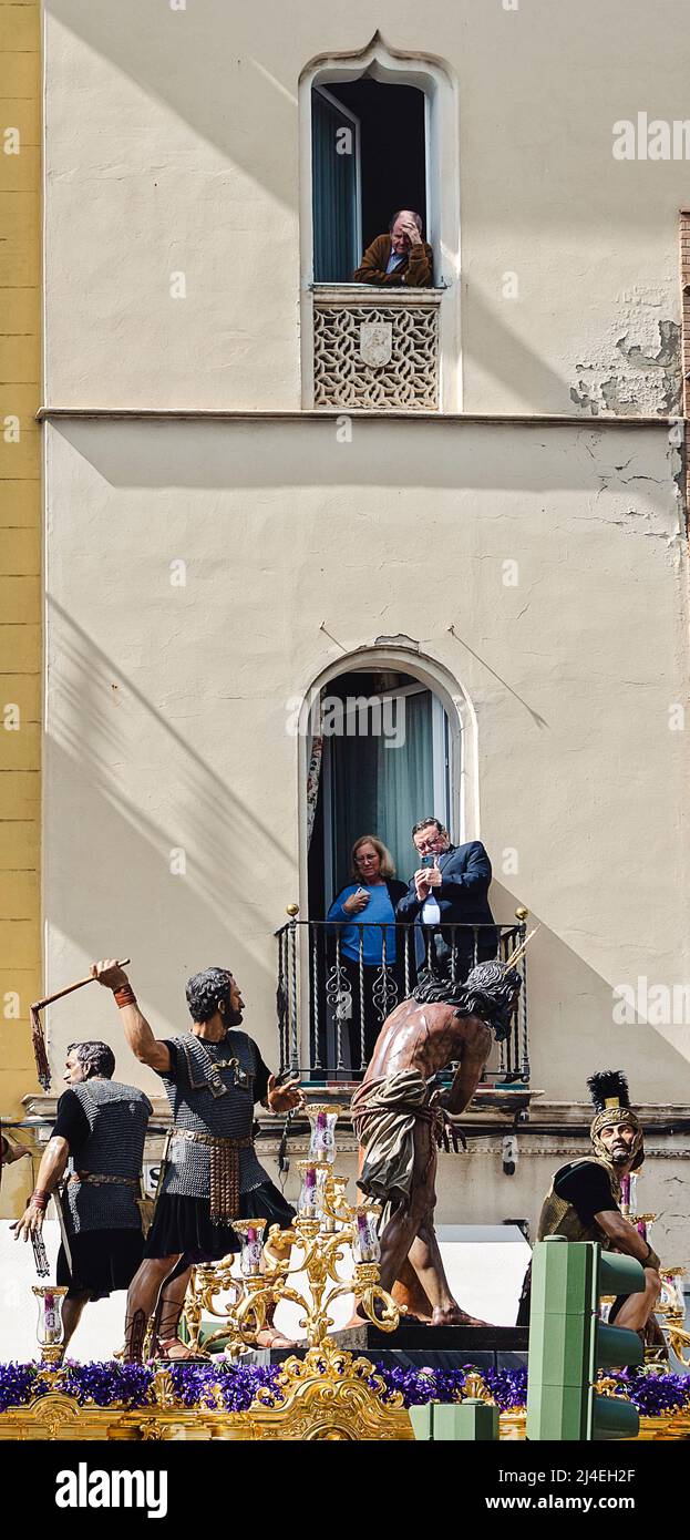 Siviglia, Spagna; 14 aprile 2022: La gente guarda una processione dai suoi balconi durante la settimana Santa. Fraternità di 'Las Cigarreras' Foto Stock