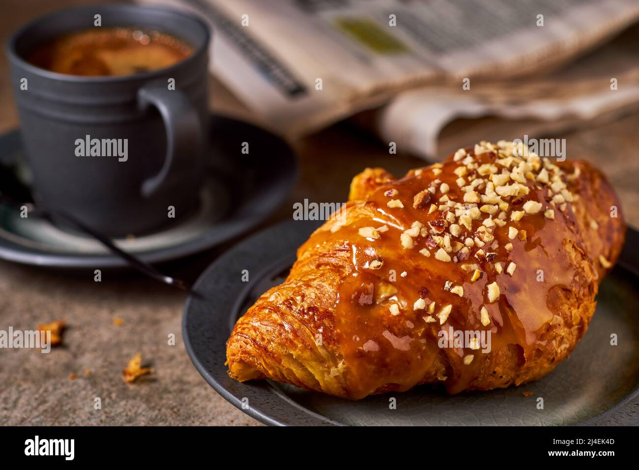 Croissant, caffè e giornale su tavola di pietra scura Foto Stock