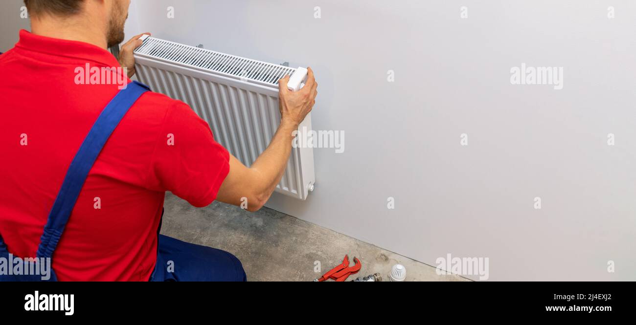 uomo che installa il radiatore di metallo bianco sulla parete. impianto di riscaldamento casa. spazio copia Foto Stock