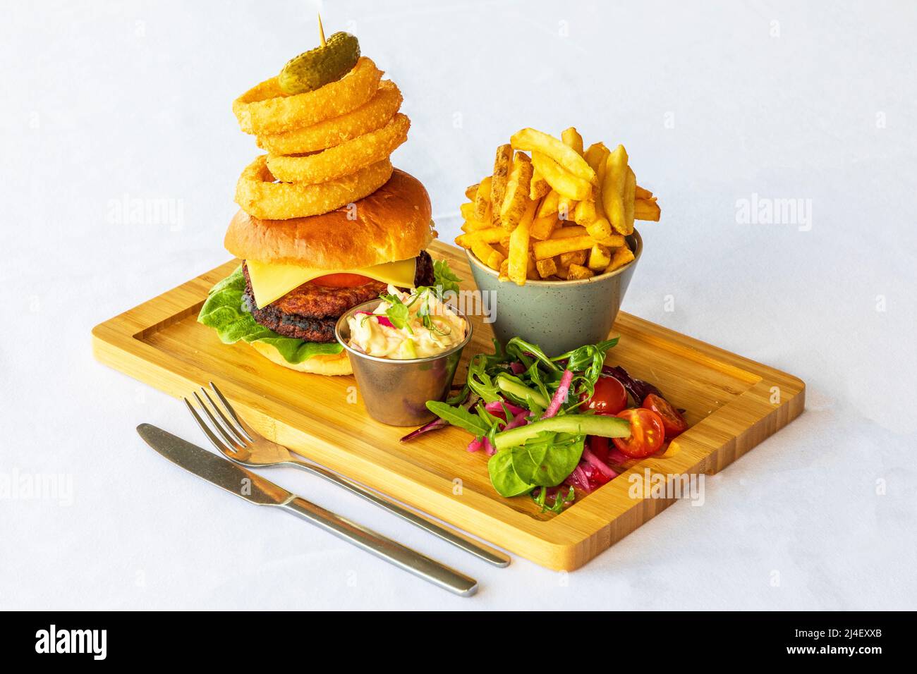 Server in legno con hamburger di manzo, anelli di cipolla, insalata francese con patate fritte e insalata laterale Foto Stock