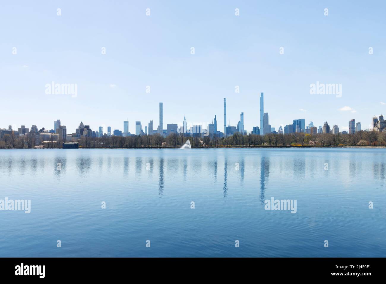 Panorama dello skyline della fila di miliardari visto attraverso il bacino idrico di Central Park con il geyser al centro con un cielo blu chiaro Foto Stock