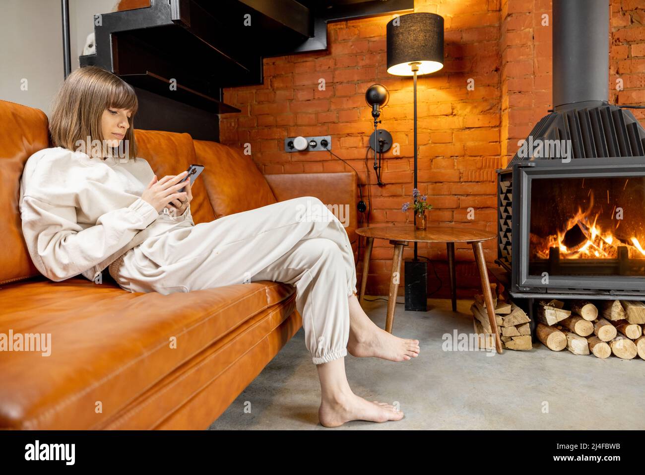 Donna seduta rilassata su un divano e utilizzando il telefono a casa Foto Stock
