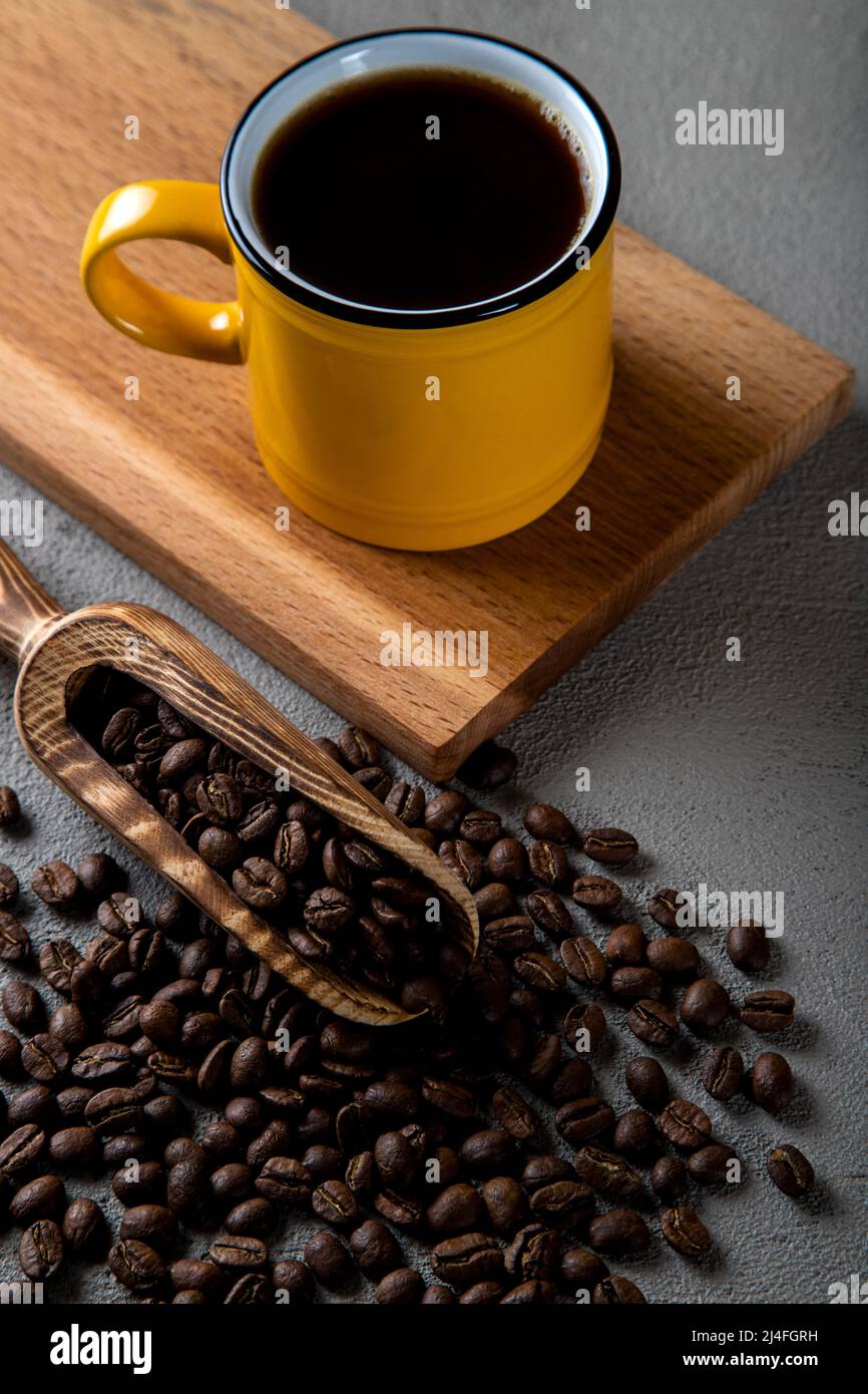 Tazza di caffè gialla con chicchi di caffè su fondo di cemento Foto Stock