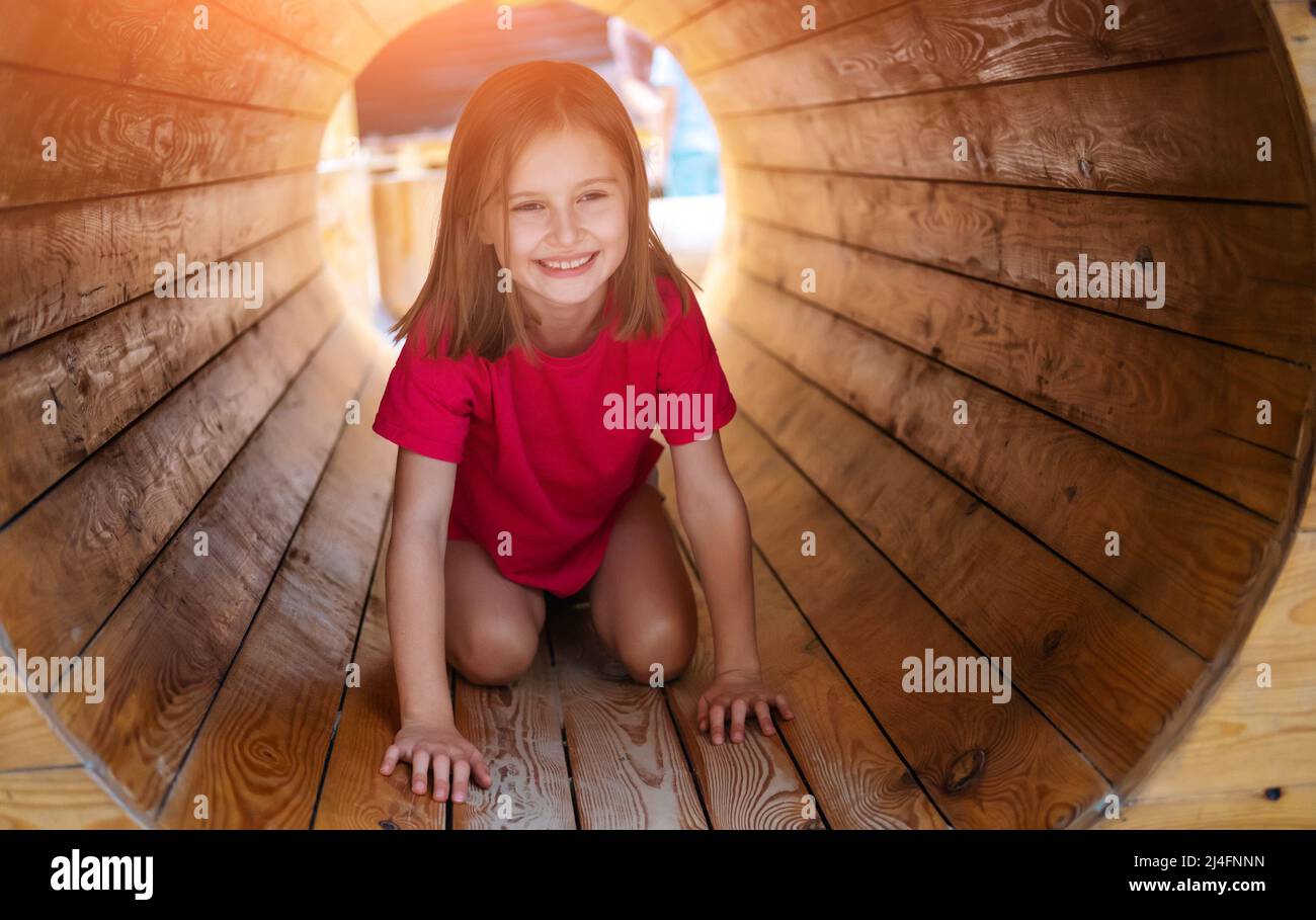 Bambina che striscia da sola all'interno del tubo di legno sul parco giochi per bambini Foto Stock