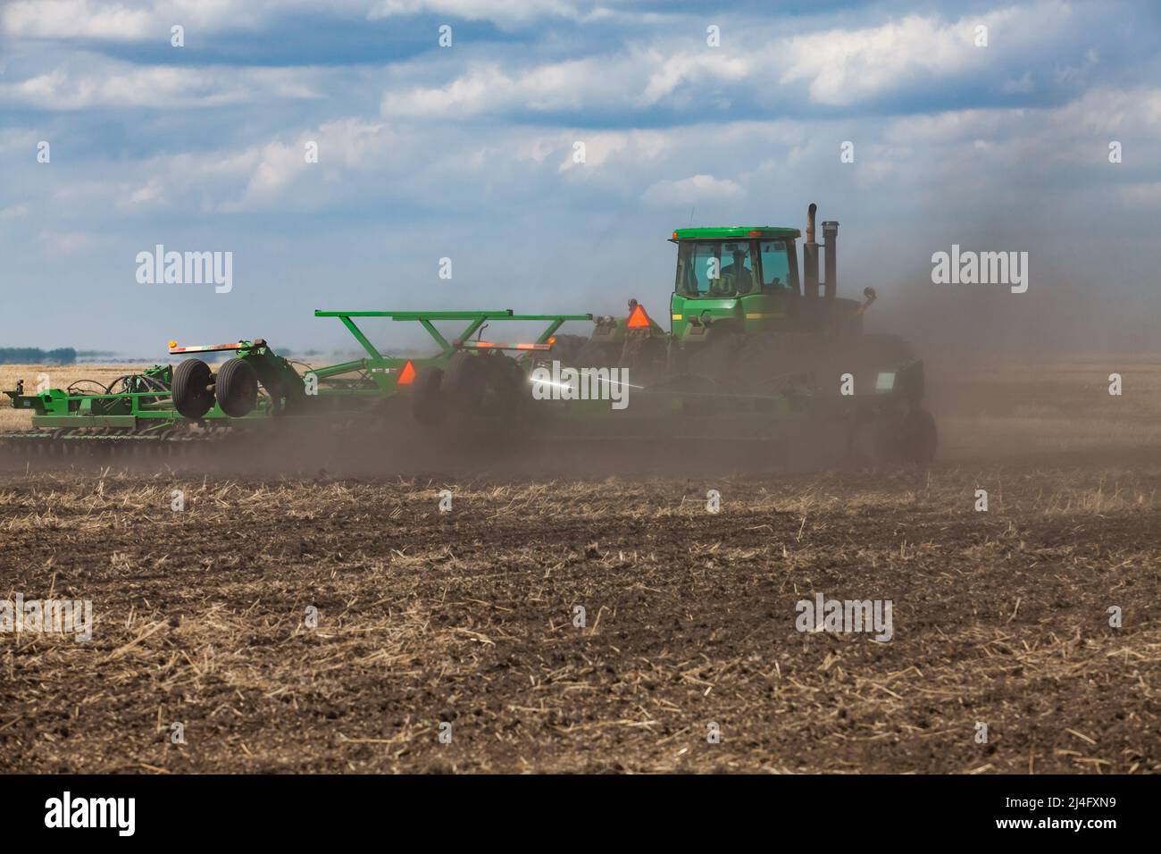 Provincia del Kazakistan settentrionale, Kazakistan - 12 maggio 2012: Campagna di semina. Trattore John Deere per la coltivazione del terreno con aratro. Nuvola di polvere. Cielo blu con nuvole Foto Stock