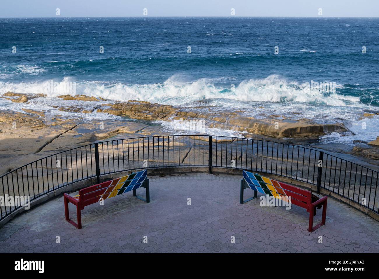Panchine dipinte in colori maltesi tradizionali e surf breaking in una ventosa giornata invernale a Sliema Malta Foto Stock