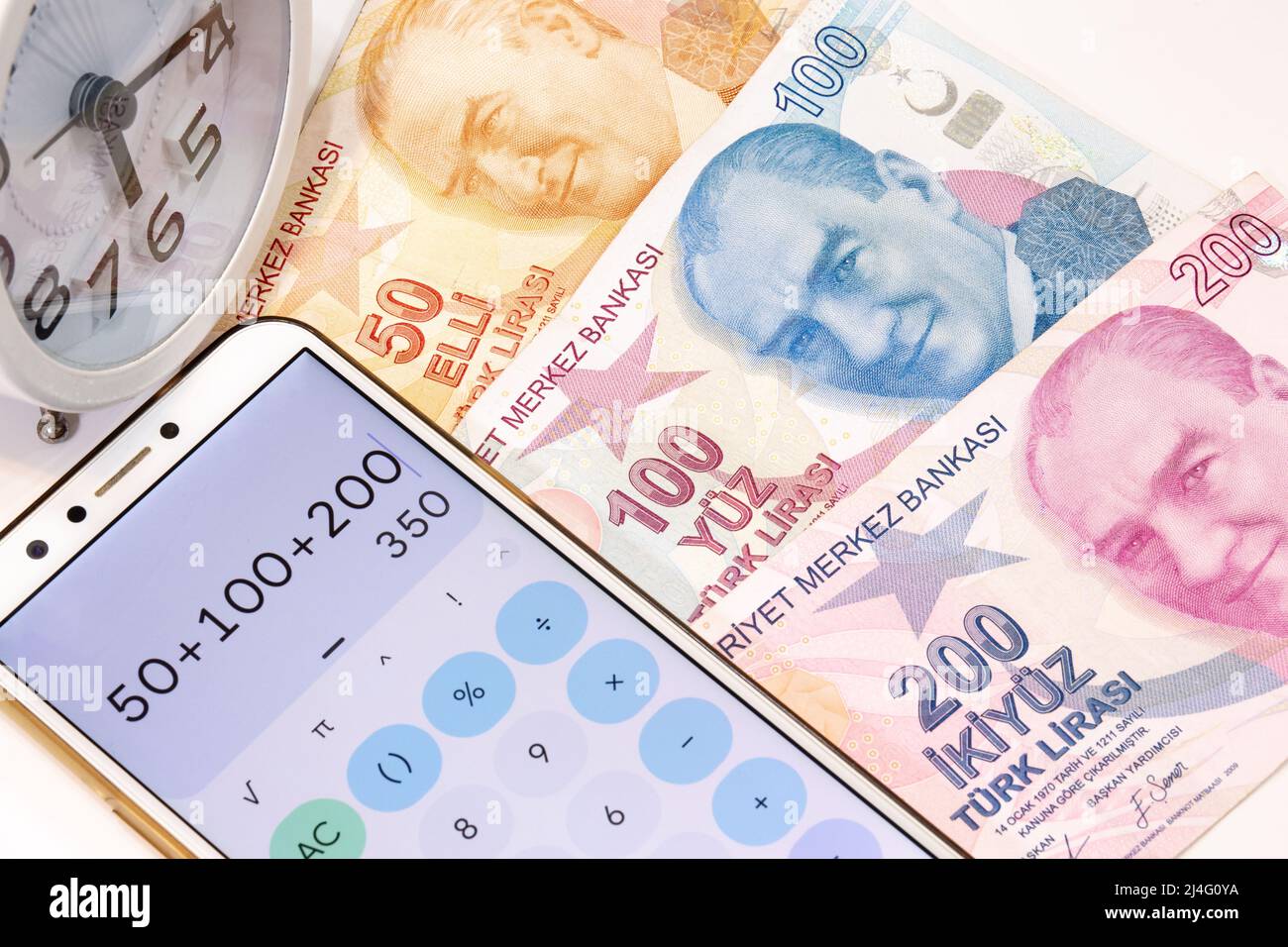 Vista dall'alto di 50, 100 e 200 banconote turche Lira, sveglia e calcolatrice app Apri cellulare su sfondo isolato. Foto Stock