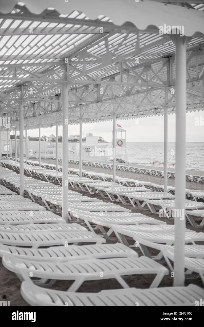 Sedie a sdraio sulla spiaggia vicino al mare. Resort vuoto. Chaise lounge - mobili da spiaggia per l'estate. Lettini sulla costa sabbiosa del mare. Chaise longue in plastica bianca pieghevole. Foto Stock