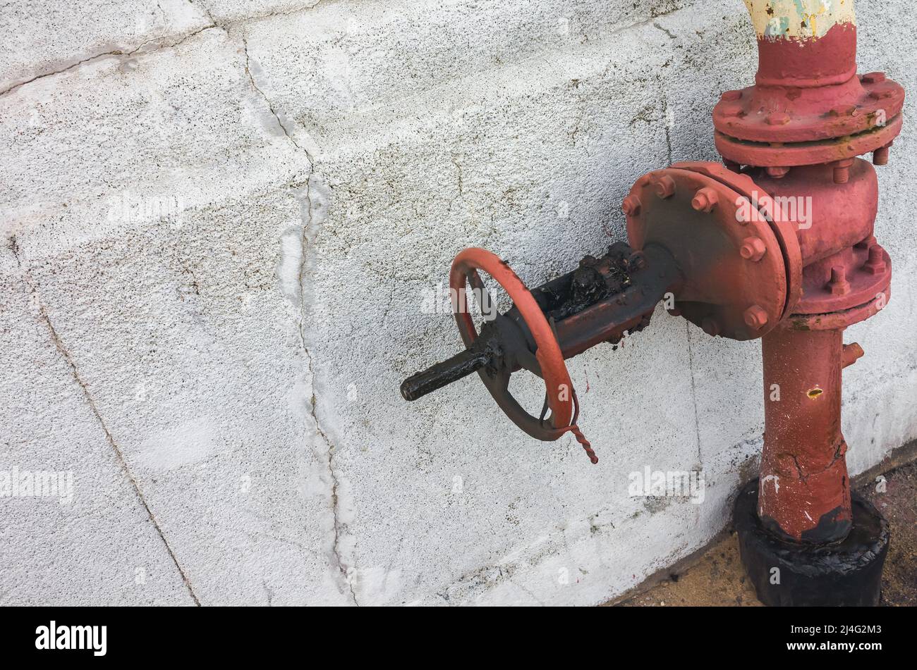 Valvola del gas rossa bloccata montata vicino alla parete di cemento grigio, foto in primo piano Foto Stock