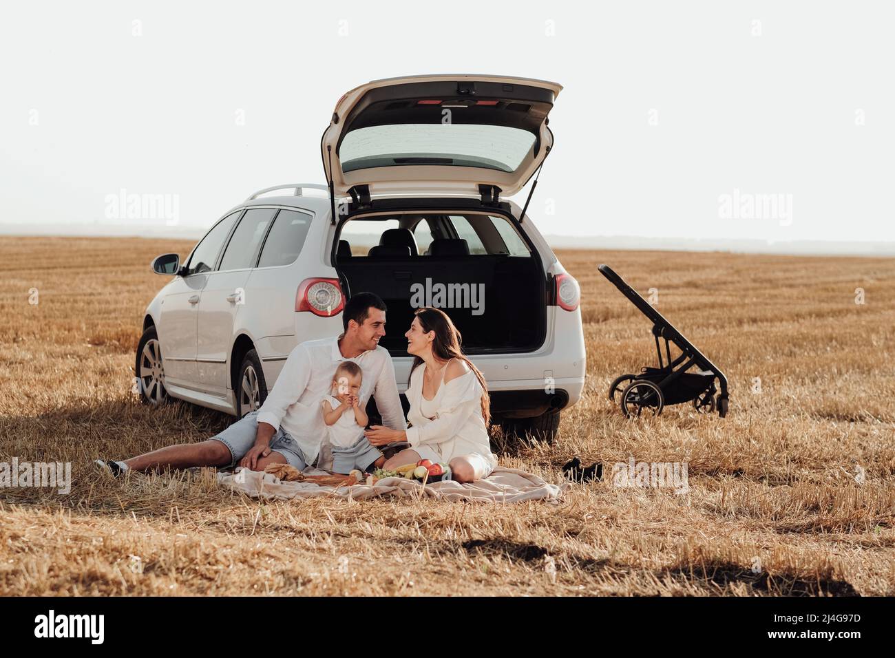 Viaggio in auto nel weekend, famiglia giovane con bambino piccolo con picnic fuori città, mamma e papà vestiti con loro figlia Foto Stock