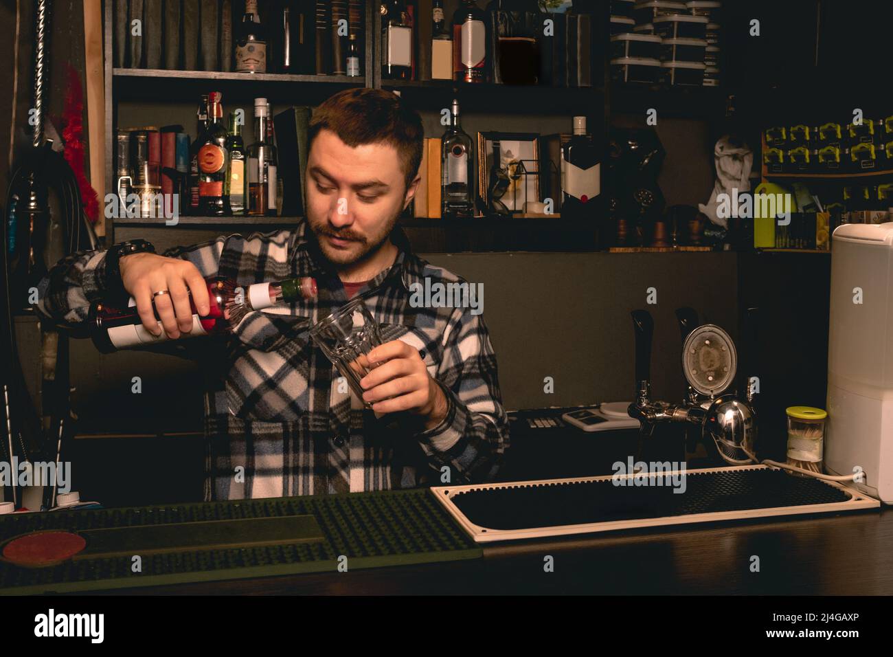 Barman preparare un cocktail dietro il bancone del bar, versando il liquore di bacche in un bicchiere Foto Stock