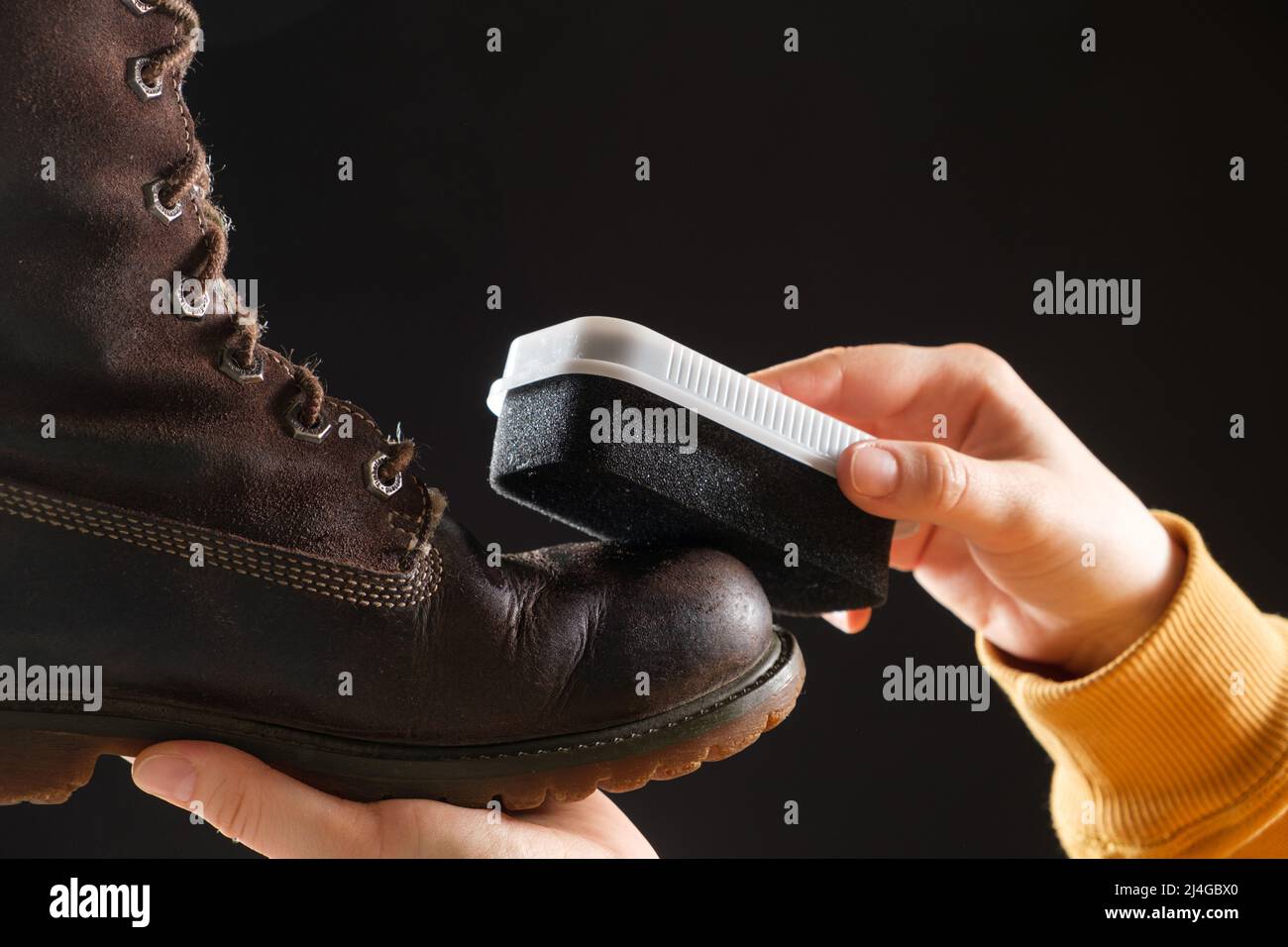La donna pulisce e applica la crema agli stivali invernali marroni nubuck  donna con una spugna. Su sfondo nero, primo piano Foto stock - Alamy
