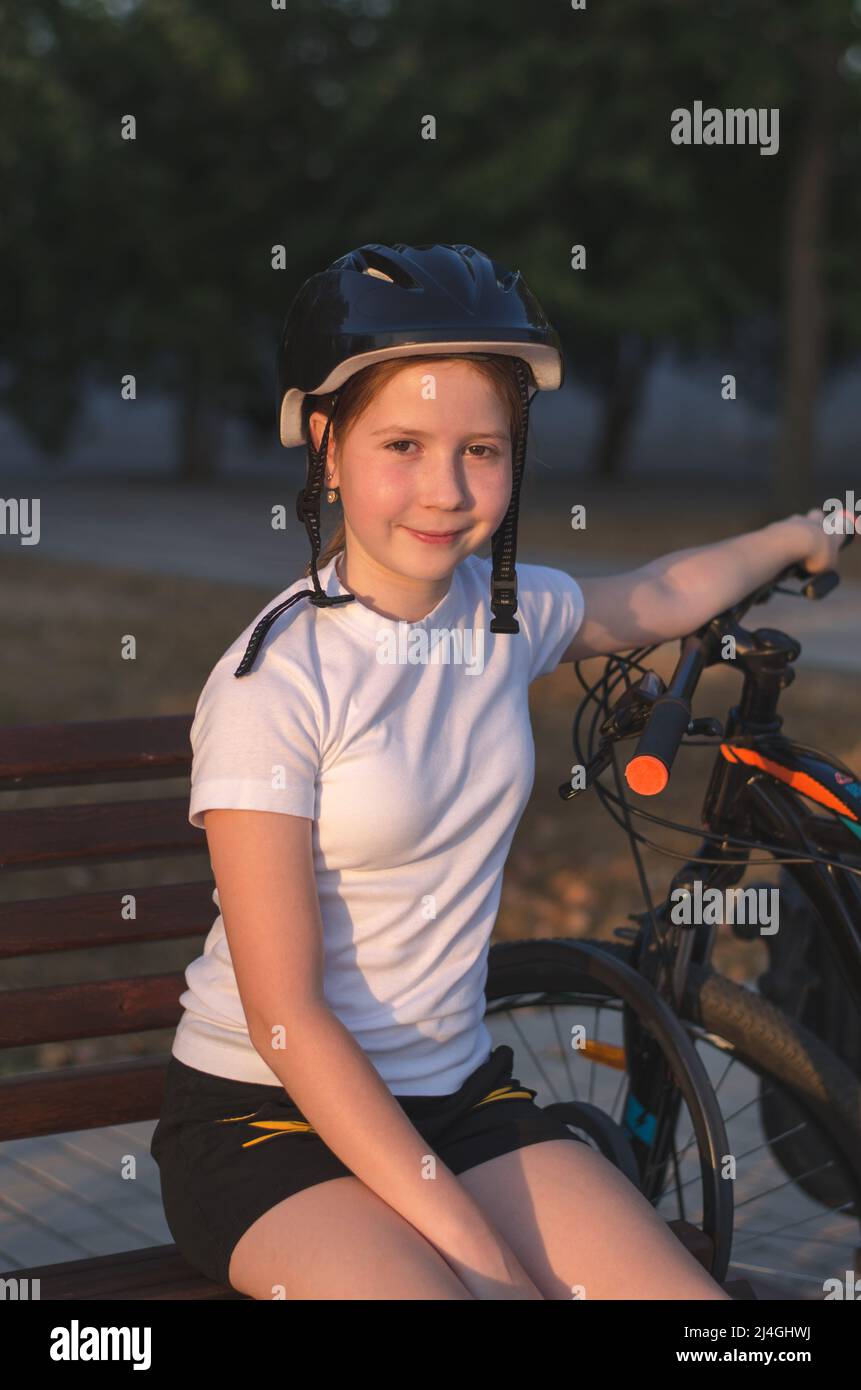 La ragazza ciclista riposa nel parco su una panchina. Atleta adolescente che riposa nel parco al tramonto Foto Stock