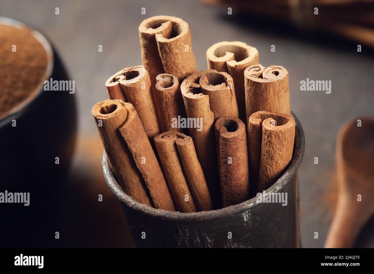 Bastoncini di cannella e ciotola di cannella in polvere sullo sfondo. Messa a fuoco selettiva. Foto Stock