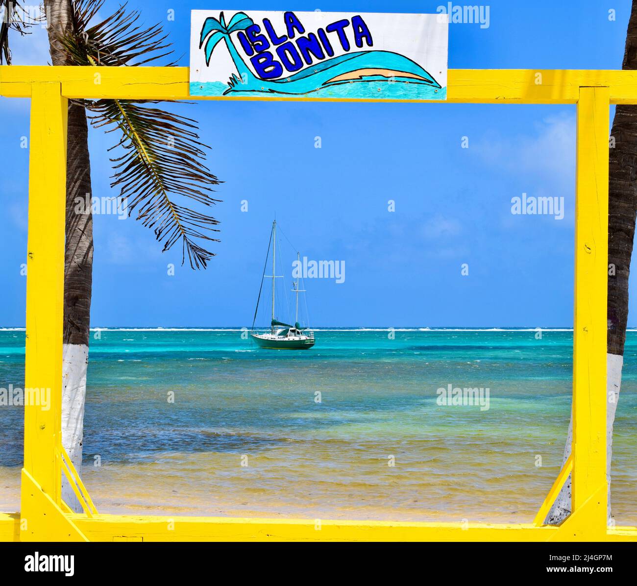 Una barca a vela nelle acque turchesi blu di San Pedro, Ambergris Caye, Belize incorniciata in un cartello 'la Isla Bonita' al parco centrale in una giornata di sole. Foto Stock