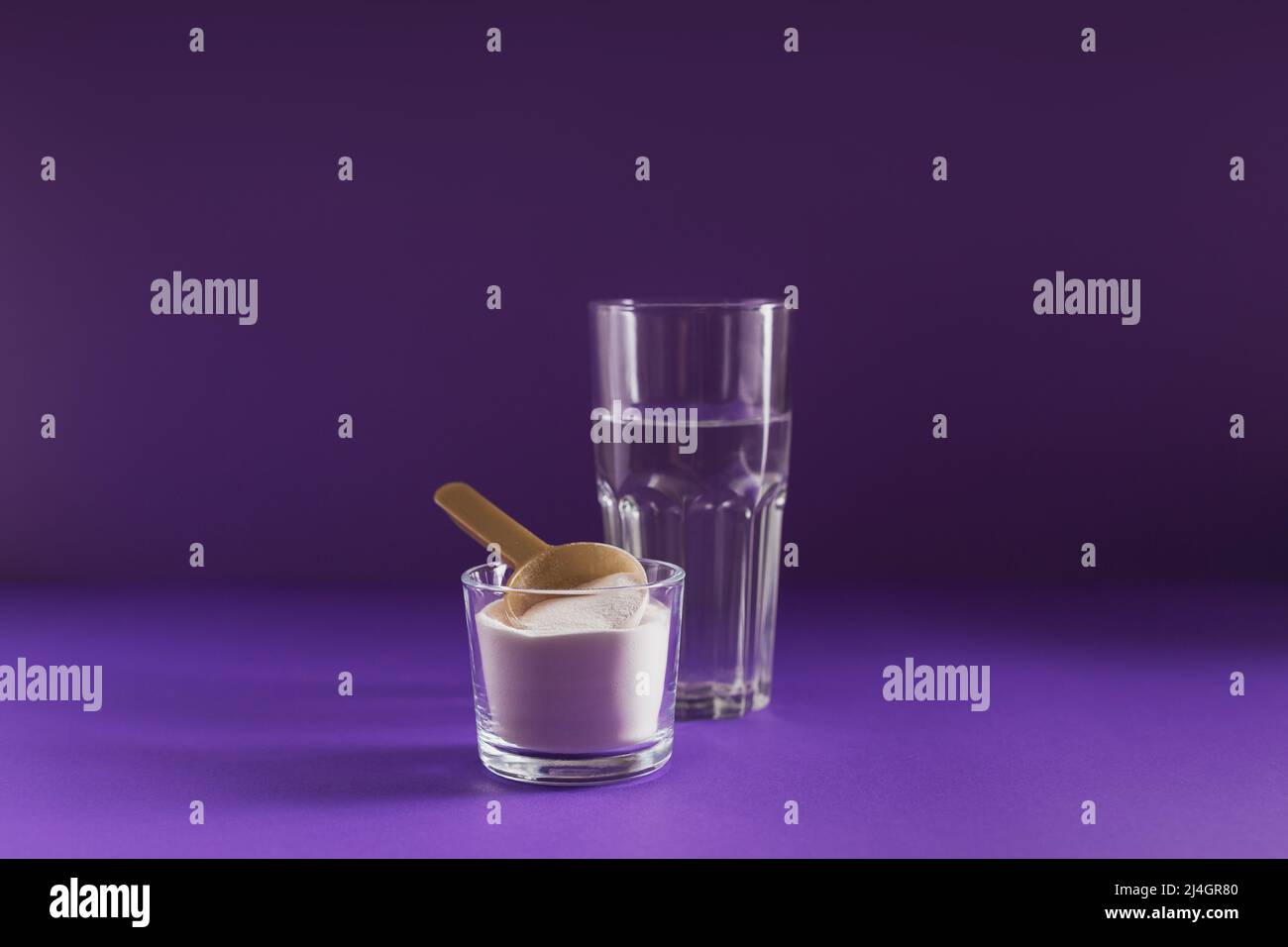 Polvere di collagene in ciotola, bicchiere d'acqua e misurino il cucchiaio su sfondo viola Foto Stock