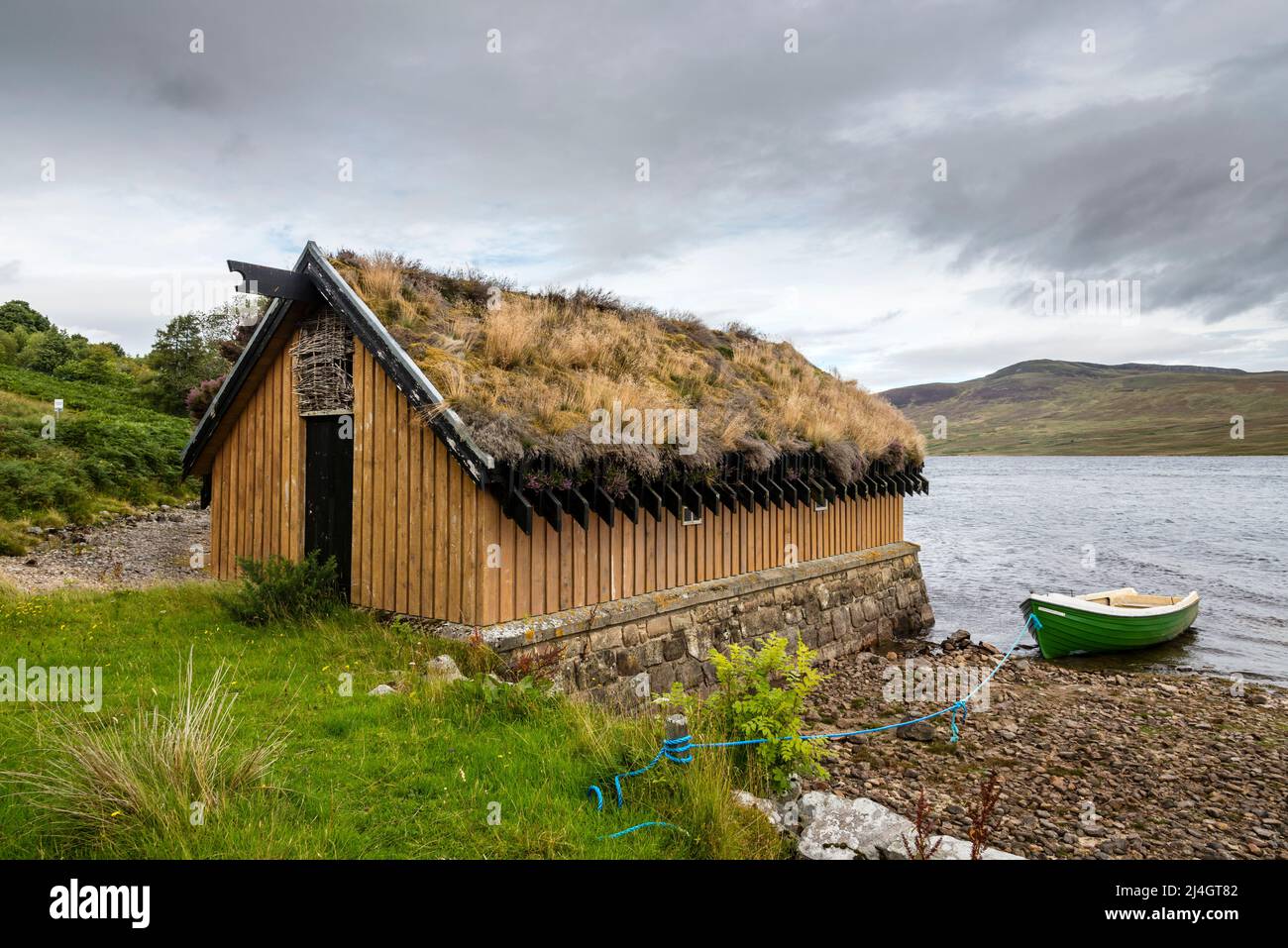 Una boathouse in legno con un tetto di erba sintetica accanto a Loch leale in una giornata nuvolosa. Foto Stock