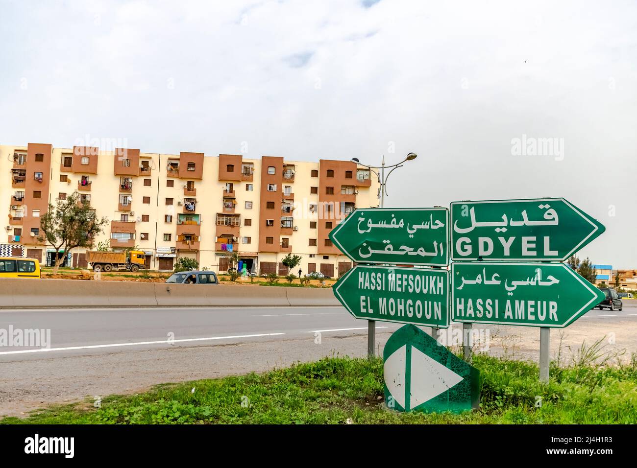 Cartello stradale di Gdyel, Hassi Amer, El Mohgoun e Hassi Mefsoukh. Caratteri arabi e francesi. Incrocio autostradale e edifici abitati. Foto Stock