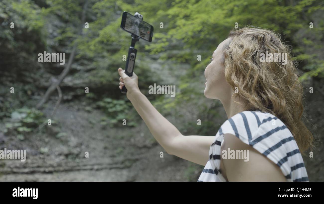 Donna prende belle viste di montagna al telefono con stabilizzatore. Azione. Scatti professionali al telefono grazie al cavalletto palmare stabilizzante. Manuale Foto Stock
