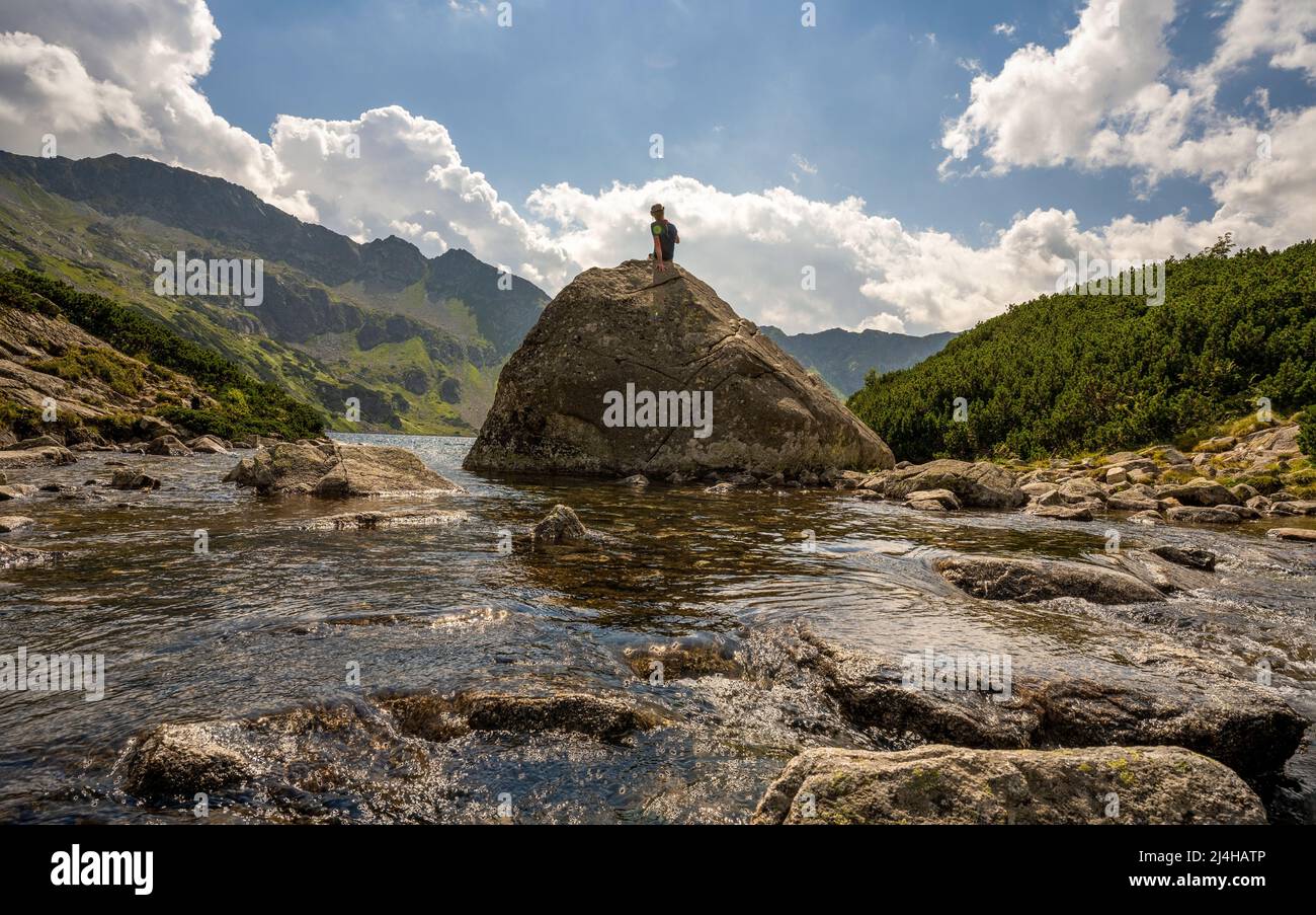 Zakopane, Polonia - 14 agosto 2021: Un uomo turistico con cappello seduto su una roccia gigante in mezzo ad un fiume torrente nell'Alto Tatra nella Valle del Fi Foto Stock