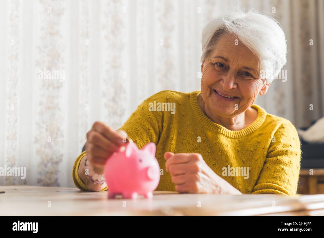 let's risparmiare denaro - bella donna anziana mettendo una moneta in piggy banca medio closeup camera di risparmio concetto. Foto di alta qualità Foto Stock