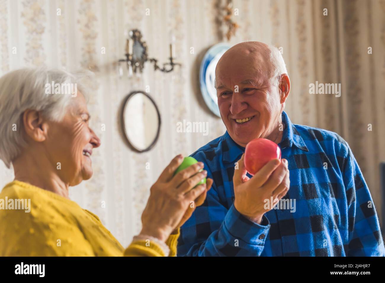 Adorabile sorridente coppia caucasica senior in un appartamento vecchio stile che si guarda l'un l'altro e sorridendo mentre tiene mele fresche. Foto di alta qualità Foto Stock