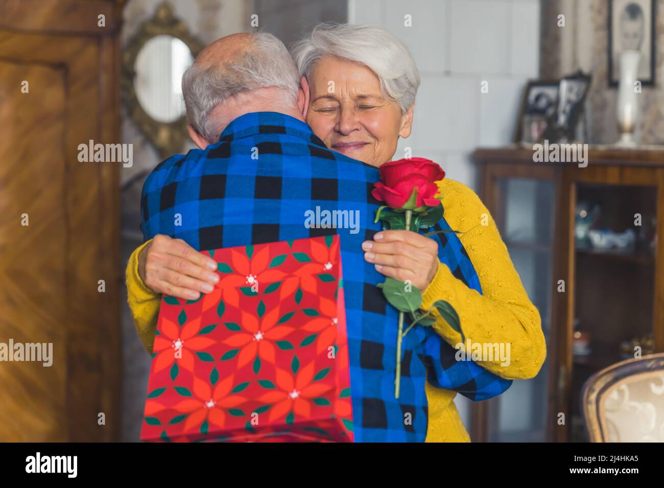 Due persone che si abbracciano. La coppia caucasica anziana festeggia il compleanno, le valentine, o l'anniversario. Nonna amichevole è abbracciato da suo marito mentre tiene regali. Foto di alta qualità Foto Stock