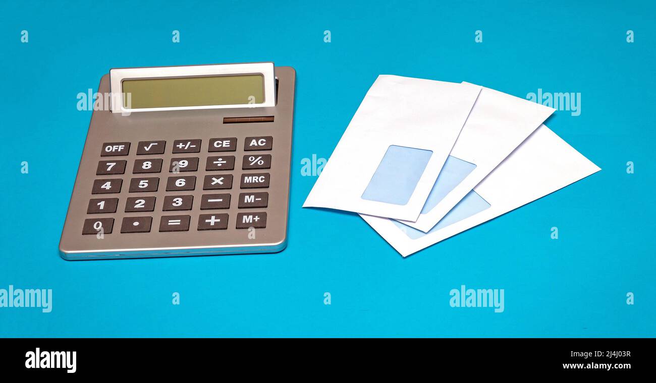 Pila di buste bianche bianche accanto alla calcolatrice elettrica su sfondo blu Foto Stock