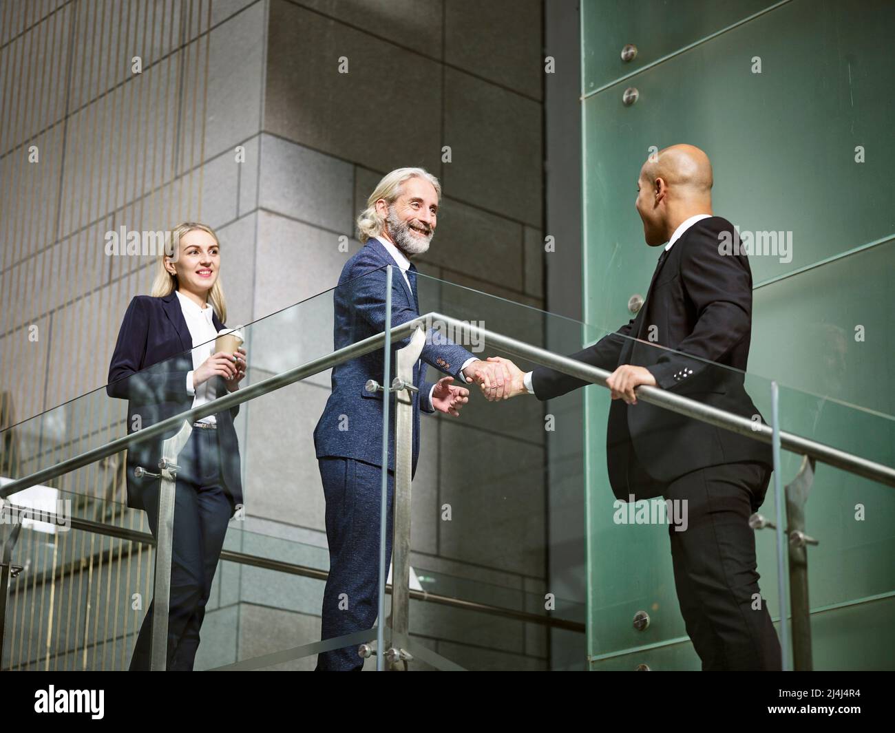 Multietnica aziendale dirigenti stringono le mani in un ufficio moderno edificio, basso angolo di visione. Foto Stock