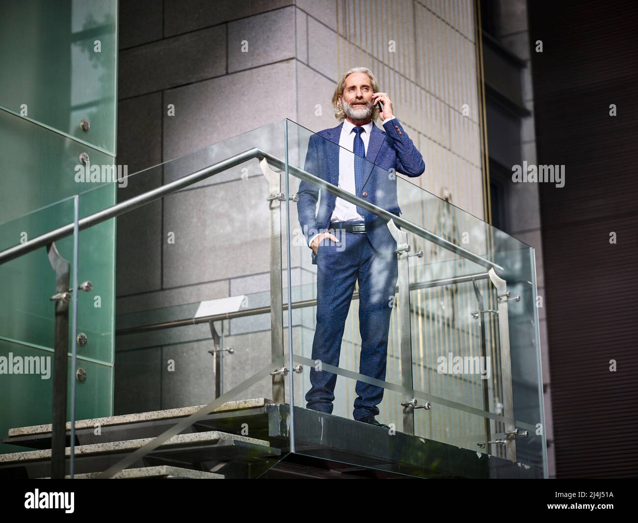 uomo d'affari caucasico maturo in piedi in cima alle scale facendo una chiamata utilizzando il cellulare in un moderno edificio d'ufficio Foto Stock