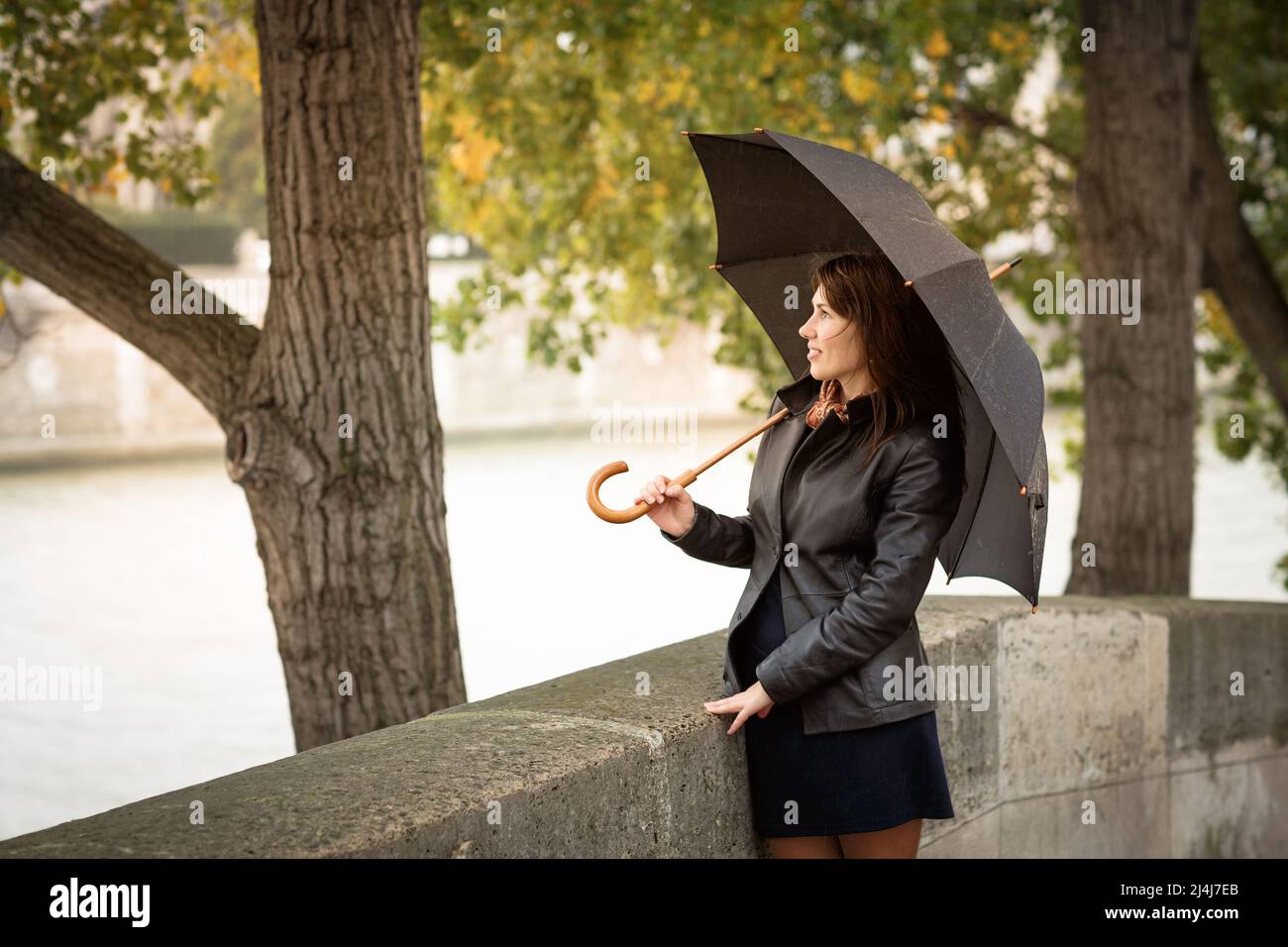 Bruna ragazza in una giacca nera si erge sul lungofiume Foto Stock