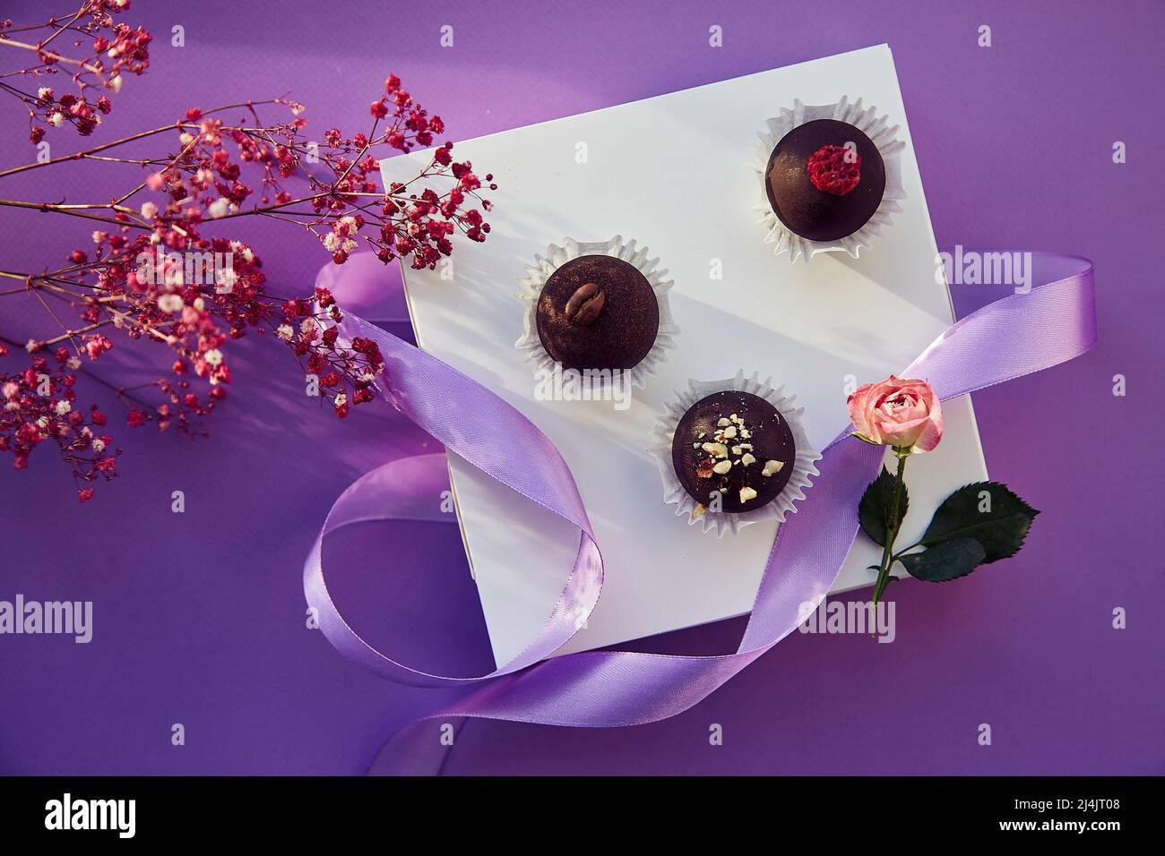 Caramelle al cioccolato festive con ombre alla moda. Delicati fiori rosa e nastro viola. Sfondo con motivo di colore viola. Foto Stock