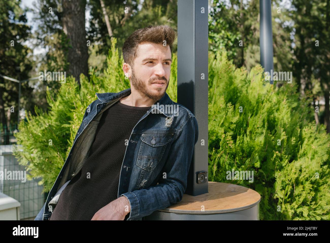 Appoggiandosi sul retro, il giovane uomo si appoggia sulla stazione di ricarica pubblica, stanco del calore e alla ricerca di un luogo di riposo Foto Stock