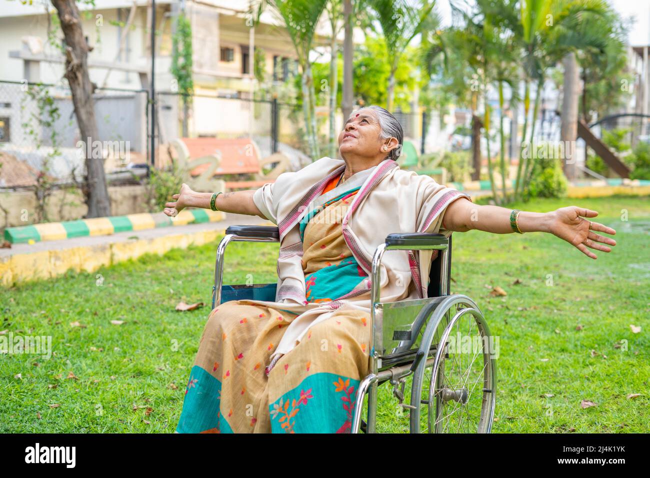 Le donne anziane felici sentono nature aria fresca allungando le braccia mentre si siedono su sedia a rotelle in giardino dopo essere usciti dall'ospedale - concetto di Foto Stock