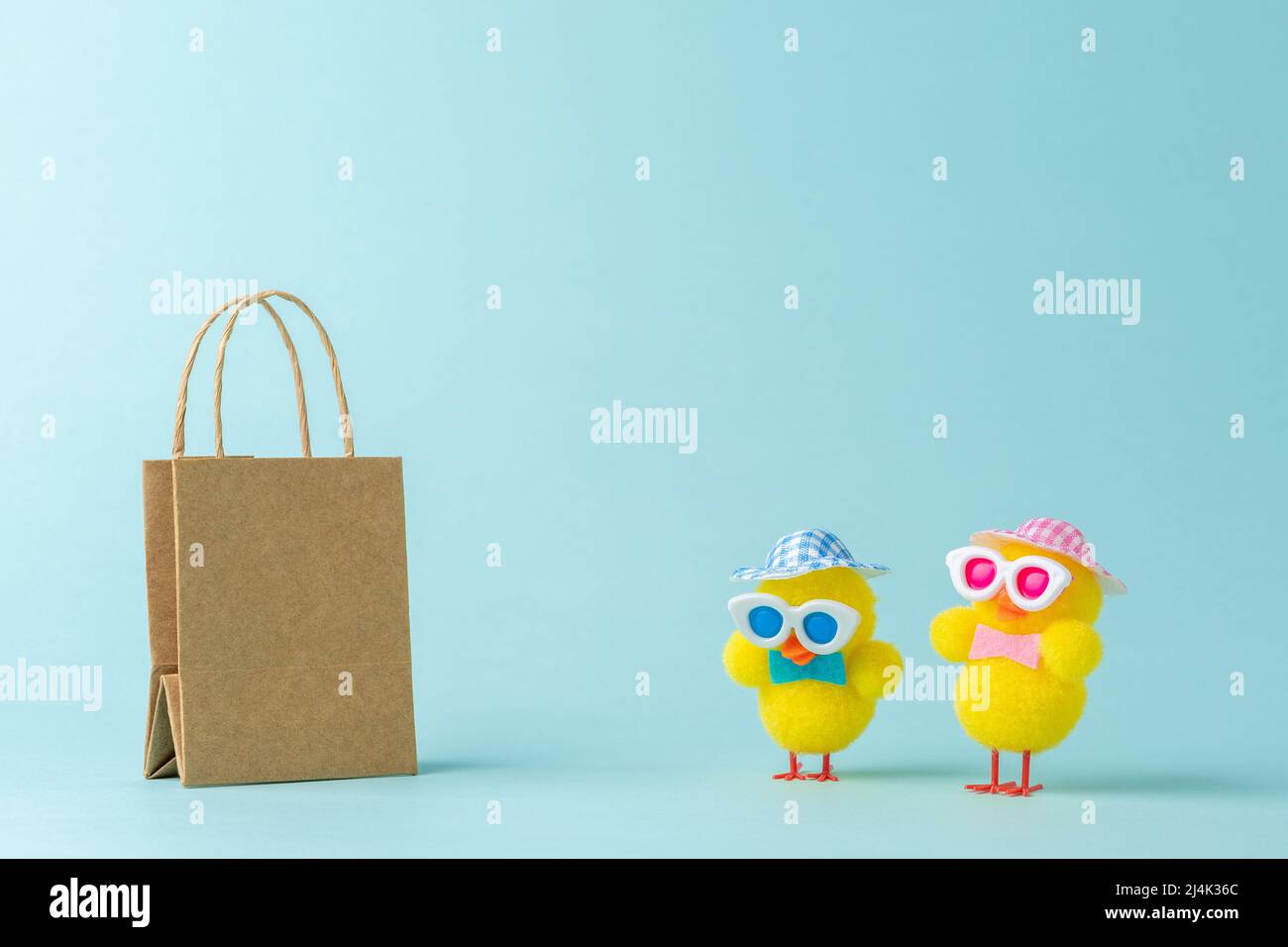 Due polli con borsa per la spesa su sfondo blu. Concetto minimo di Pasqua. Foto Stock