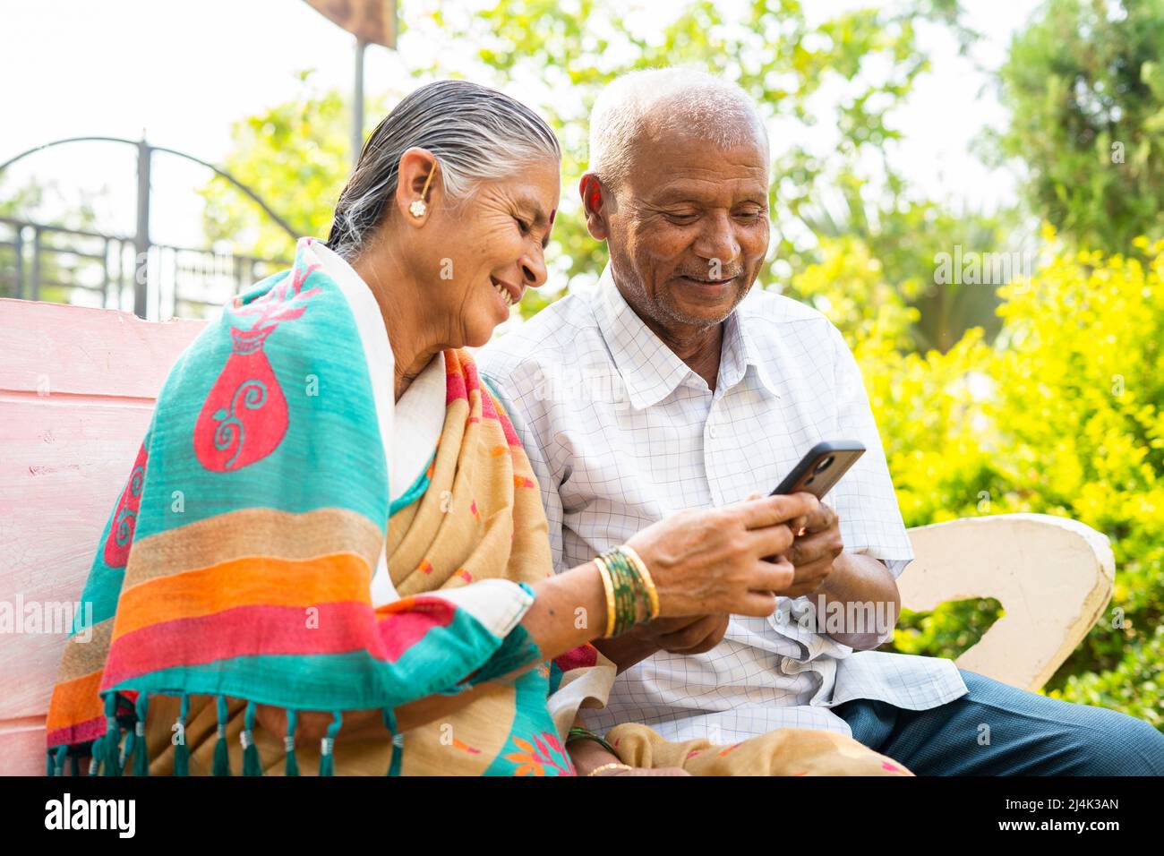 Coppia anziana che utilizza il telefono cellulare mentre si siede nel parco - concetto di social media, stili di vita tecnologici e relax Foto Stock