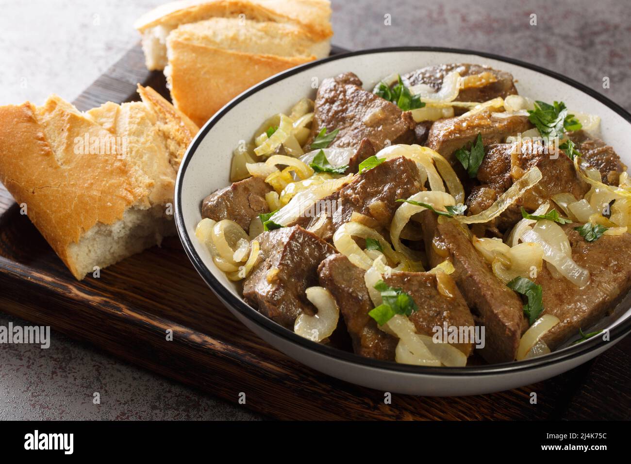 Fegato di manzo fritto con cipolle ed erbe primo piano in un piatto e pane su un vassoio di legno orizzontale Foto Stock