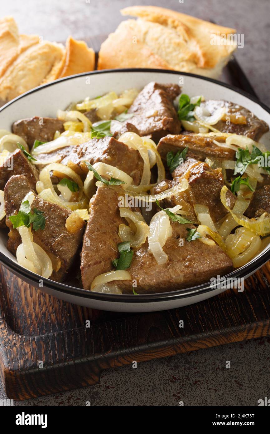 deliziosi pezzi di fegato di vitello mescolare fritto e stufato con anelli di cipolla closeup nel recipiente sul tavolo. Verticale Foto Stock