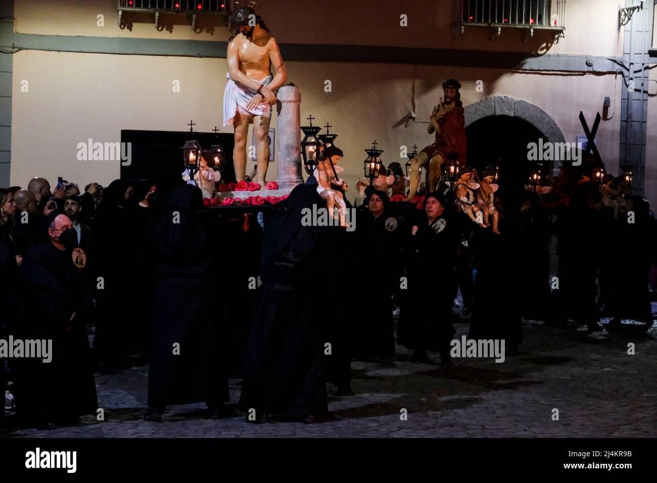 Dopo un periodo di due anni, le processioni del Venerdì Santo tornano a Sessa Aurunca il 17 aprile 2022. Gli uomini che indossano cappe nere e che sono affiliati all'Arciconfraternita della Santa Croce sfilano per le strade della città ed eseguono una 'dance' lenta e ondeggiante. È il passo rituale chiamato 'cunnulella', eseguito portando religiosamente le statue dei Misteri sulle loro spalle. Mentre passano, in vari punti si illuminano i carraciuni, enormi falò fatti da fasci raccolti e allestiti nei vari quartieri attraverso i quali passa la processione, simbolo di devozione a Cristo. Foto Stock