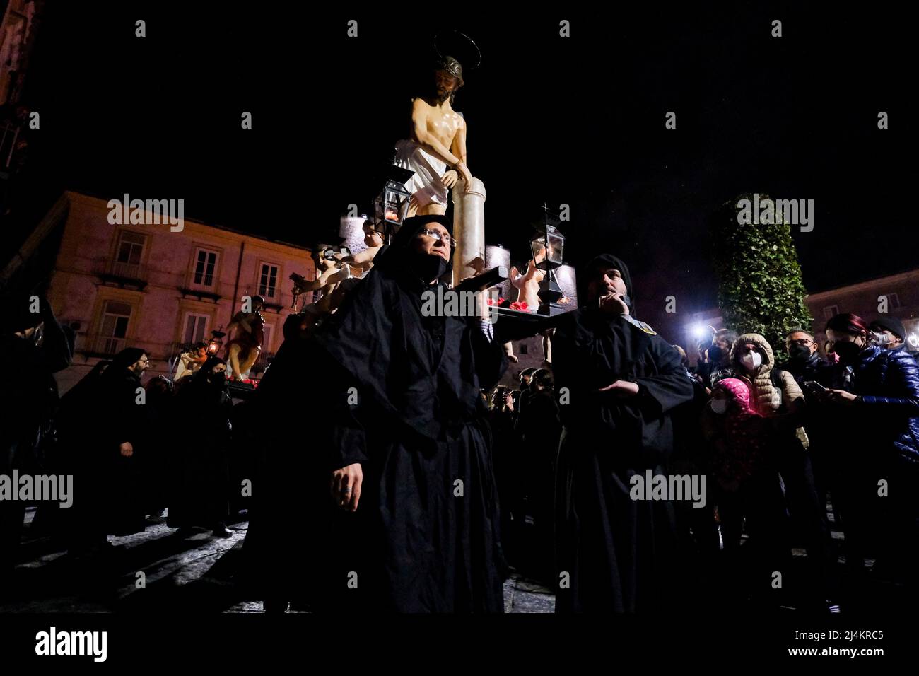 Dopo un periodo di due anni, le processioni del Venerdì Santo tornano a Sessa Aurunca il 17 aprile 2022. Gli uomini che indossano cappe nere e che sono affiliati all'Arciconfraternita della Santa Croce sfilano per le strade della città ed eseguono una 'dance' lenta e ondeggiante. È il passo rituale chiamato 'cunnulella', eseguito portando religiosamente le statue dei Misteri sulle loro spalle. Mentre passano, in vari punti si illuminano i carraciuni, enormi falò fatti da fasci raccolti e allestiti nei vari quartieri attraverso i quali passa la processione, simbolo di devozione a Cristo. Foto Stock