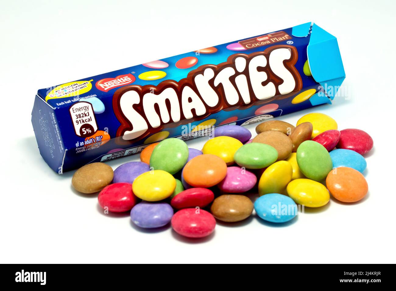 Primo piano di un tubo di Smarties con un mucchio di dolci al cioccolato multicolore e croccanti, isolati su sfondo bianco. Foto Stock