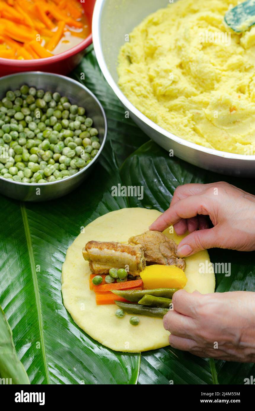 Donna autoctona cucina tipica colombiana e messicana piatto tradizionale fatto con pasta di mais e ripieno di pollo, maiale, costolette di maiale, verdure; avvolgimento Foto Stock