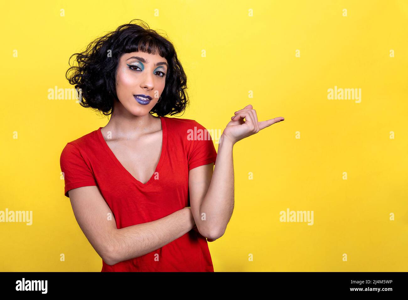 La giovane donna sorridente in t-shirt rossa punta con il dito. Ritratto donna con look alla moda e colori brillanti su sfondo giallo. Foto Stock