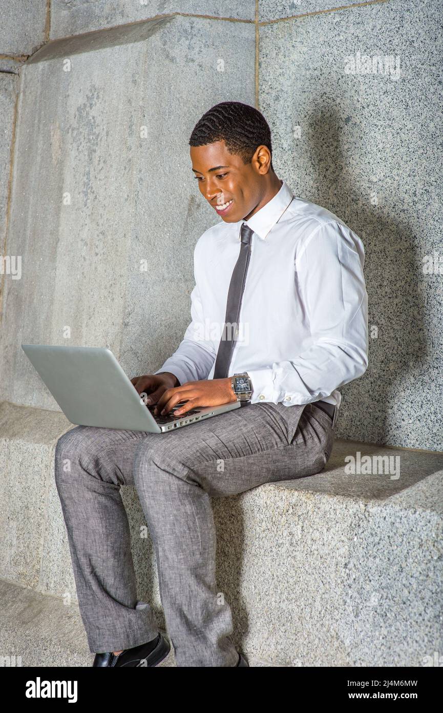Vestendo in camicia bianca, una cravatta nera, pantaloni grigi, un giovane  studente nero del college sta lavorando su un computer al di fuori di un  edificio d'ufficio Foto stock - Alamy