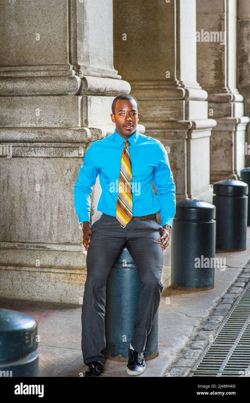 Vestendo in una camicia blu chiaro, una cravatta colorata motivo, pantaloni  grigi, scarpe in pelle, un giovane uomo d'affari nero è seduto fuori per  fare una pausa Foto stock - Alamy