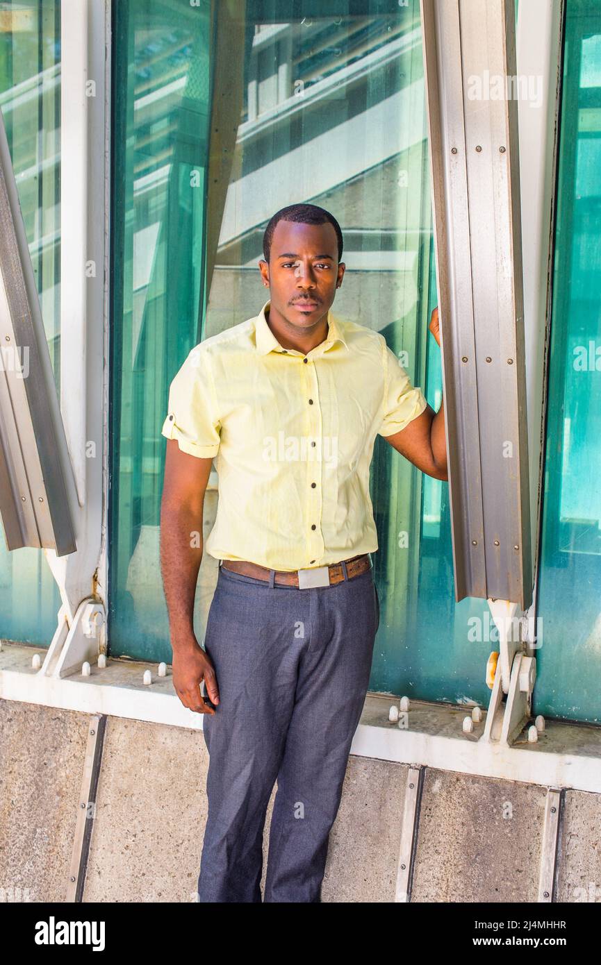 Vestendo in una camicia giallo chiaro, pantaloni grigi, un giovane  attraente ragazzo nero è in piedi da una struttura triangolare, che ti  guarda Foto stock - Alamy