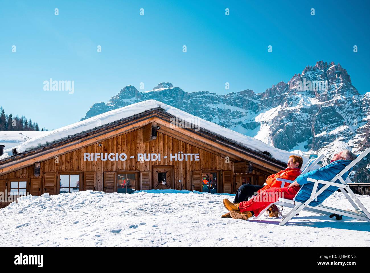 Coppia rilassante sulle sedie a sdraio accanto allo chalet in giornata di sole durante le vacanze sciistiche Foto Stock