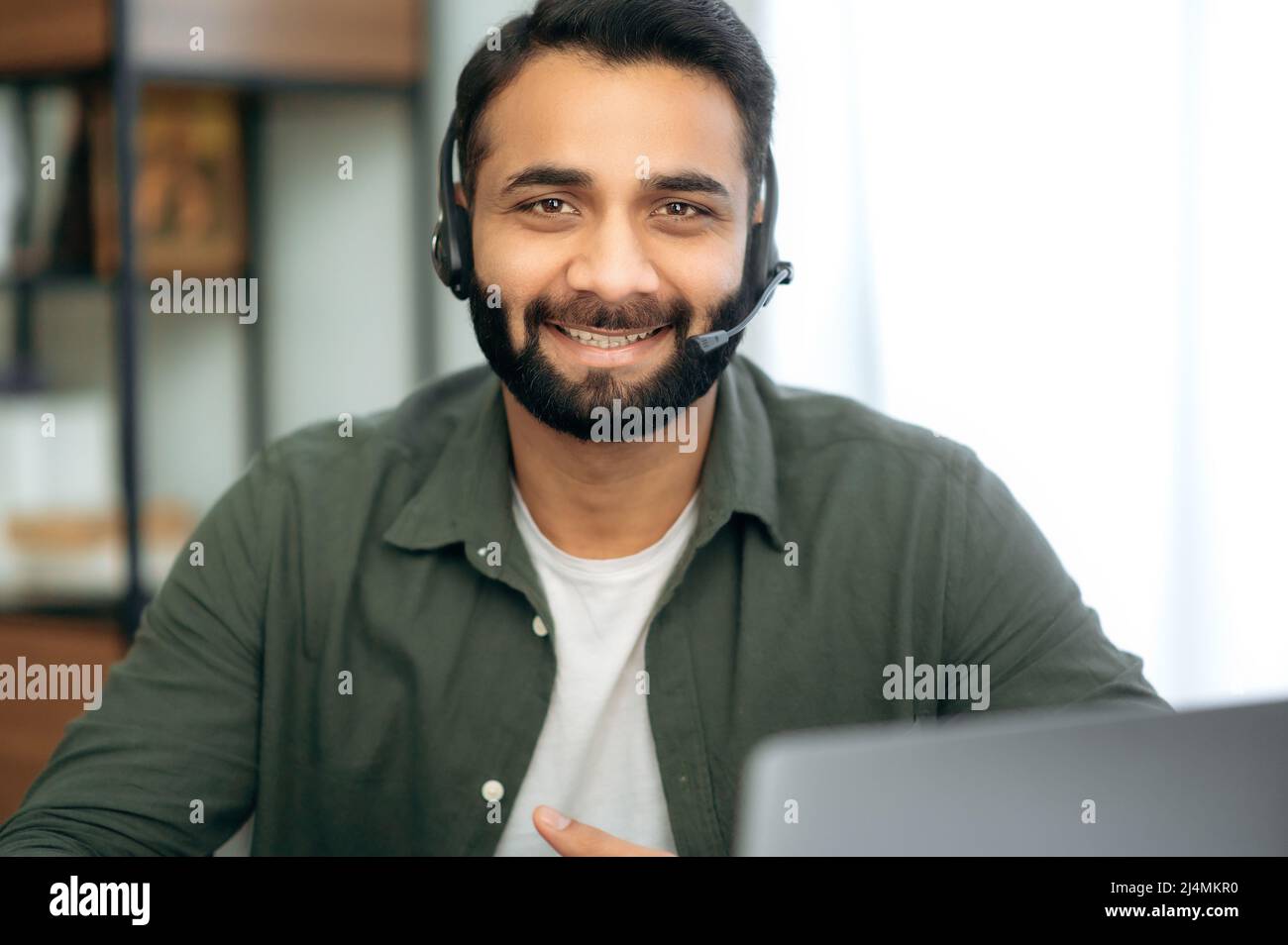 Amichevole piacevole attraente indiano o arabo uomo con cuffia, consulente o mentore, hotline esperto, guarda direttamente la macchina fotografica, sorrisi amichevole, conduce la consultazione. Concetto di servizio di supporto Foto Stock